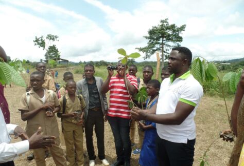 Photo de plusieurs jeunes qui plantent des arbres devant des écoliers dans le cadre du projet de reboisement dans les établissements scolaires